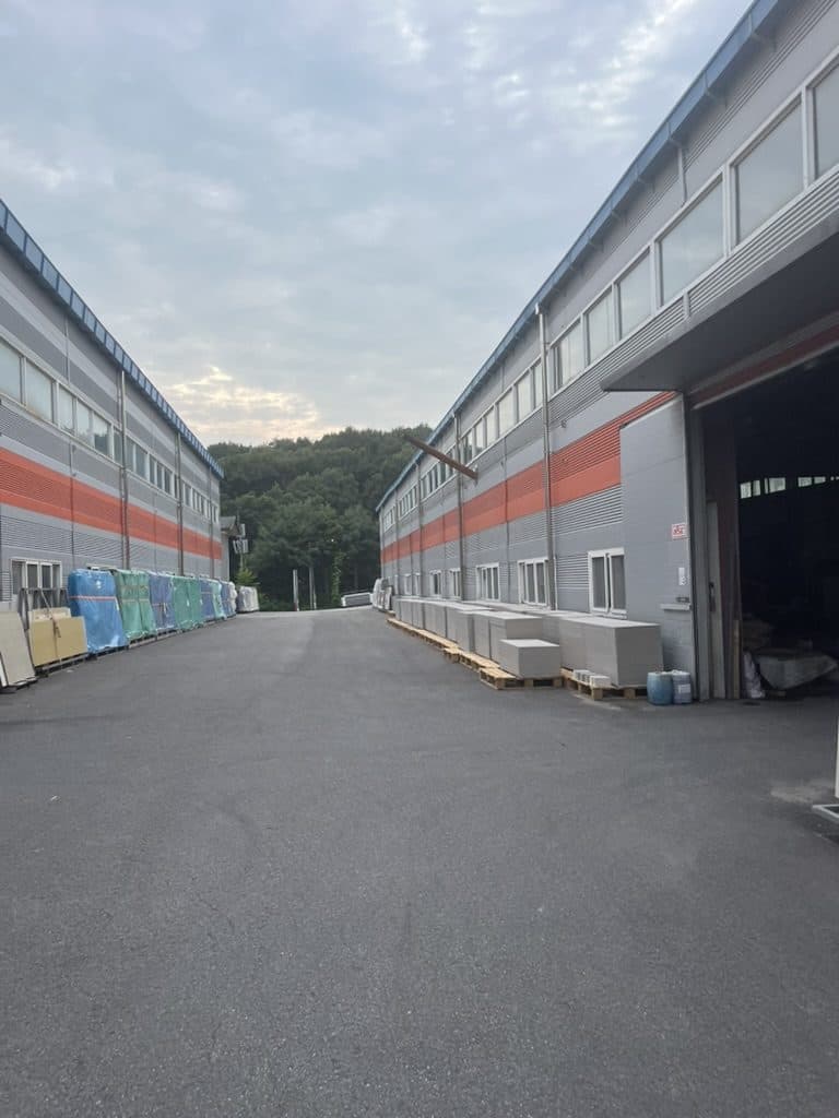 가공동(왼쪽)·창고동(오른쪽) 사이 진입로와 출고 대기 자재